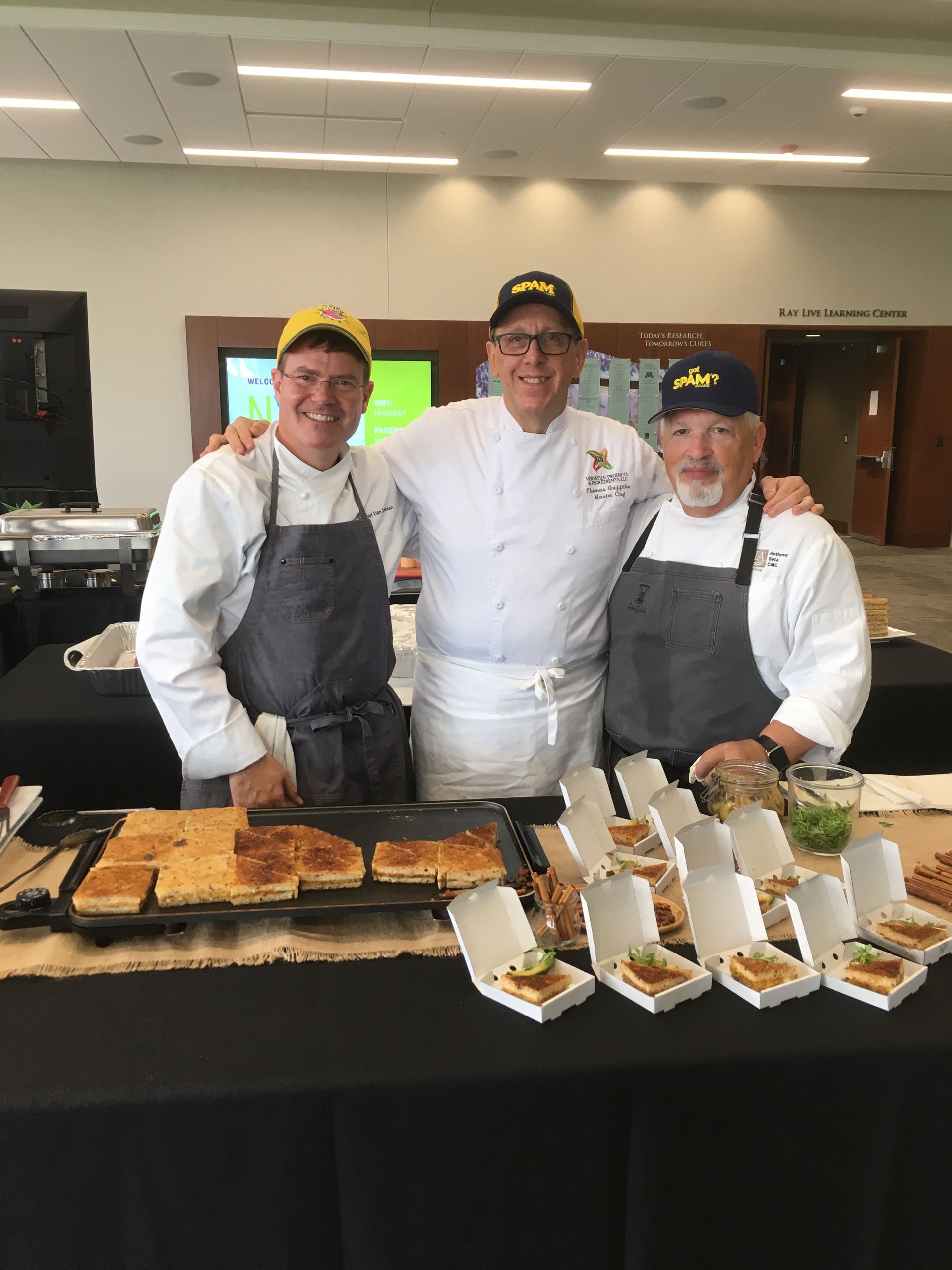 Three chefs are posing for a picture in front of a table filled with food.