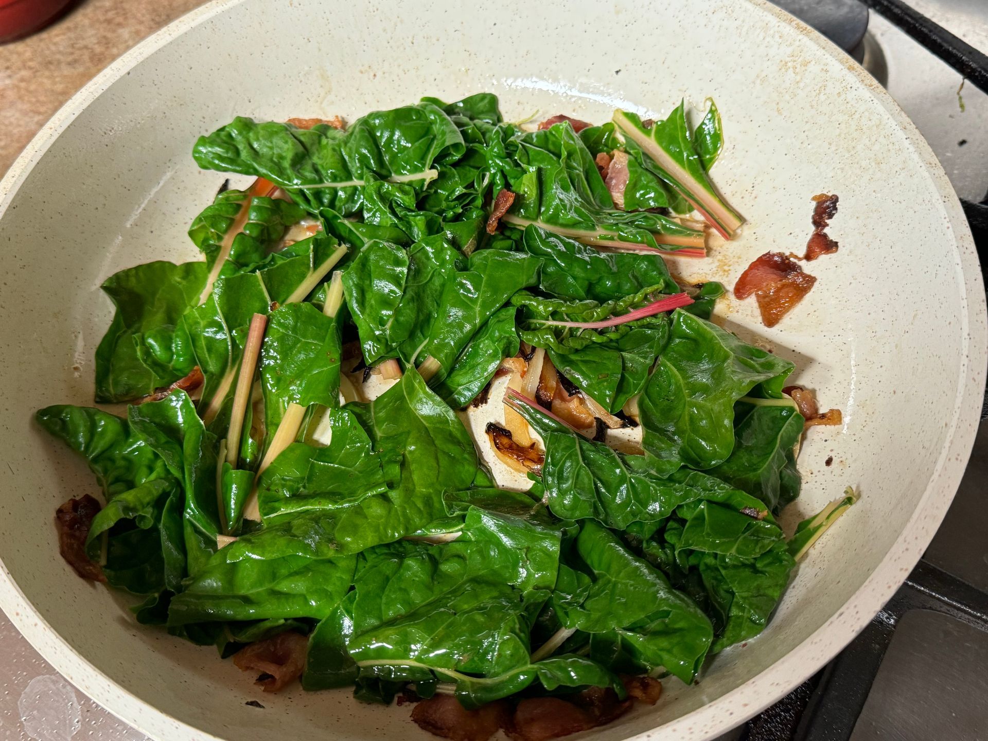 A white pan filled with spinach and mushrooms is cooking on a stove.