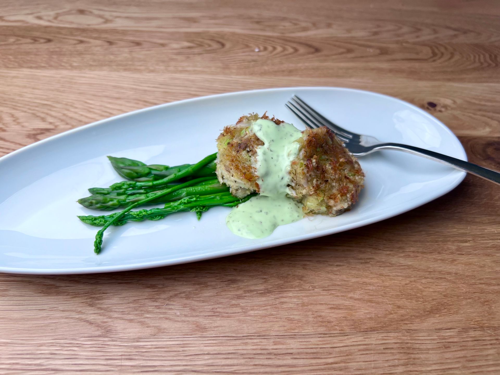 A plate of food with asparagus and a fork on a wooden table.