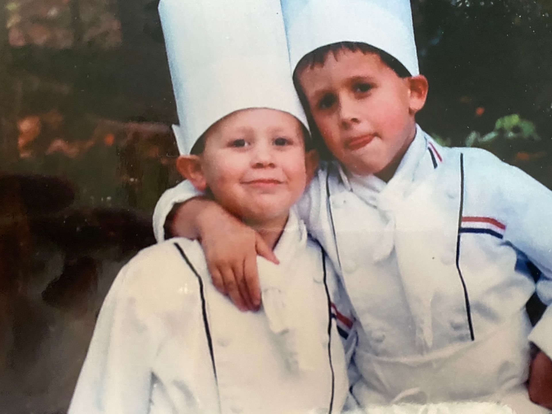 Two young boys wearing chef hats and aprons pose for a picture