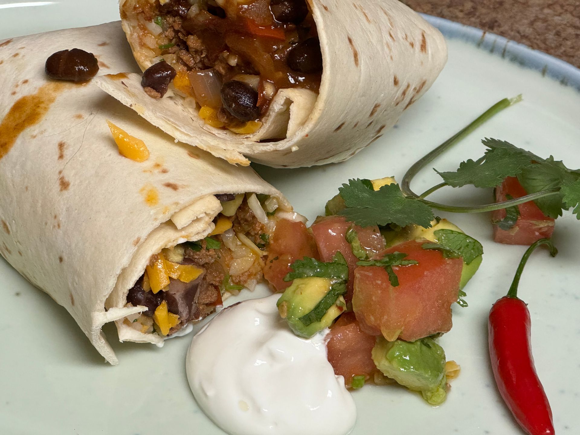 A burrito on a plate with guacamole and sour cream