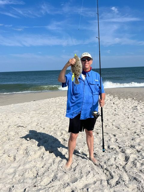 A man is standing on a beach holding a fish and a fishing rod.