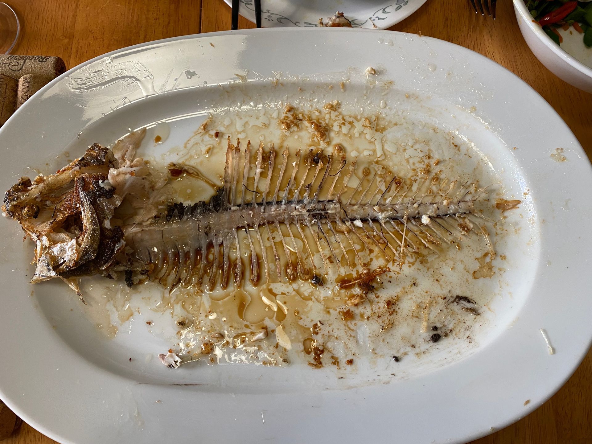 A white plate topped with a fish skeleton on a wooden table.