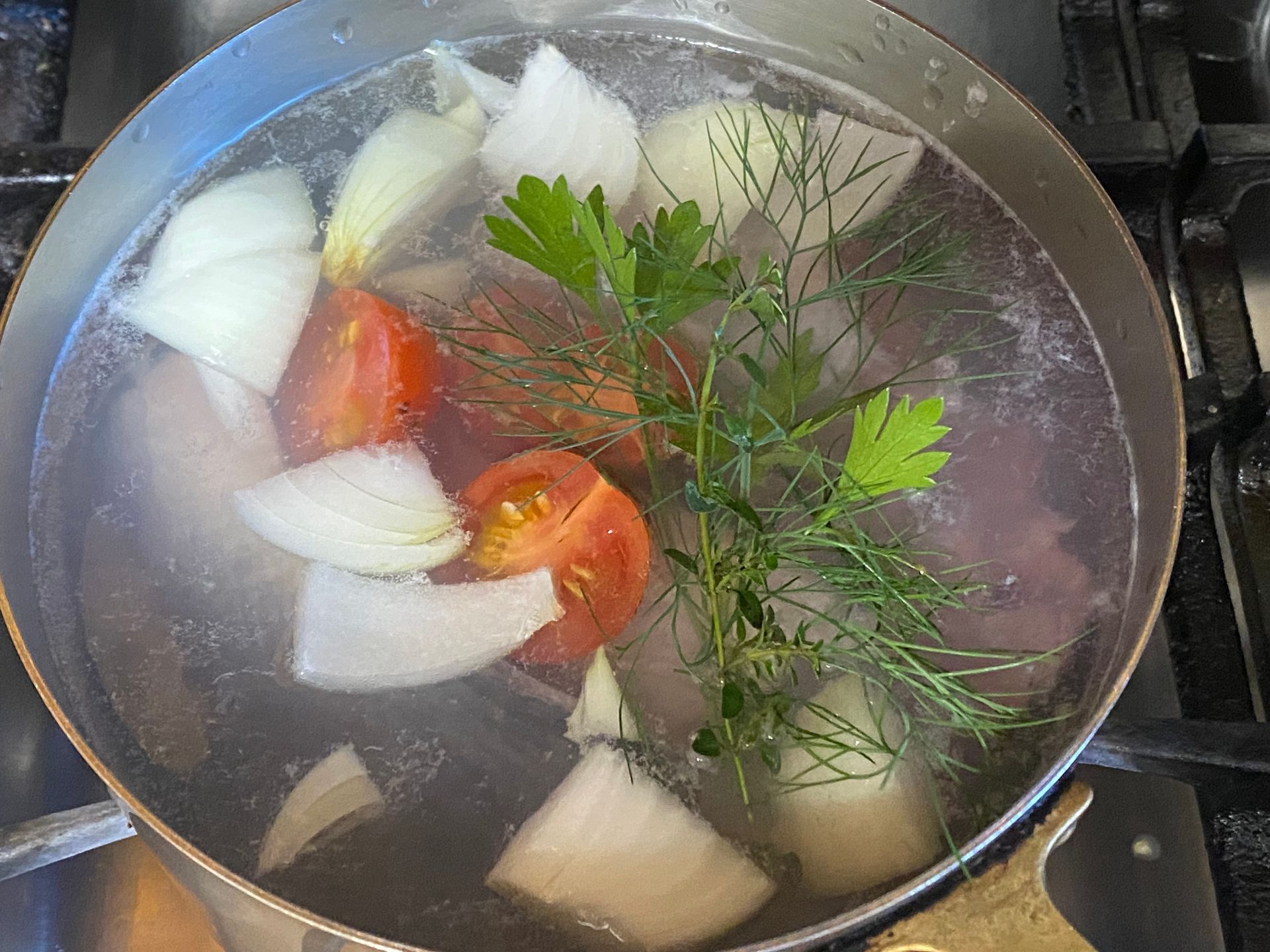 A pot of boiling water with tomatoes , onions and parsley in it.