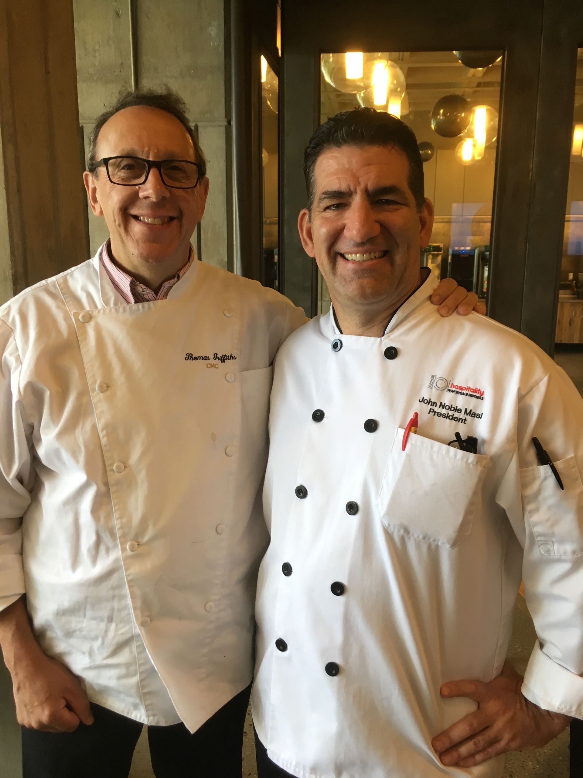 Two men in chef jackets are posing for a picture