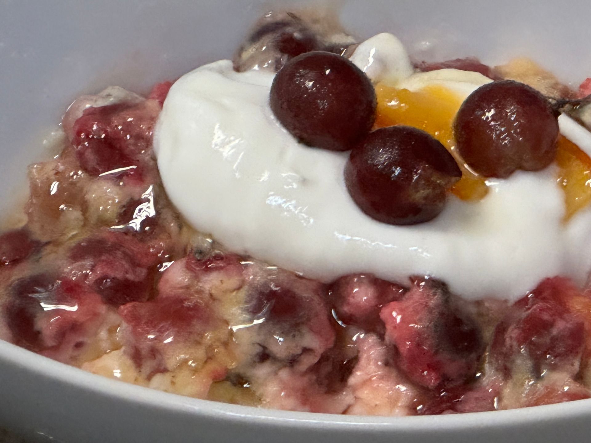 A bowl of oatmeal with whipped cream and cherries on top