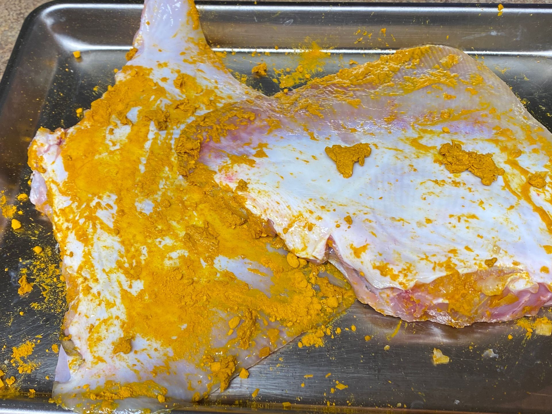 A piece of meat is covered in yellow powder on a metal tray.