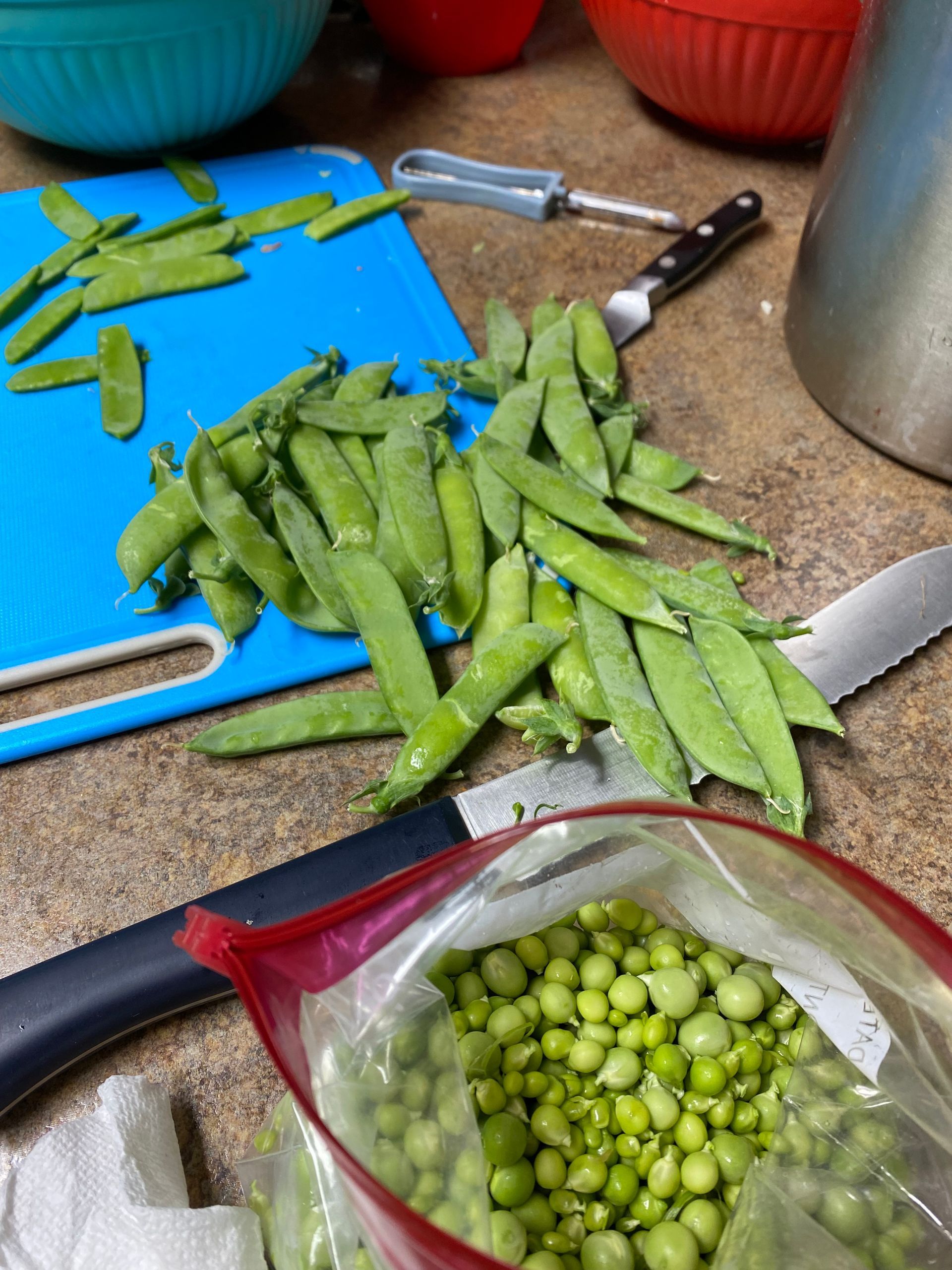 A bag of peas is sitting on a counter next to a cutting board.