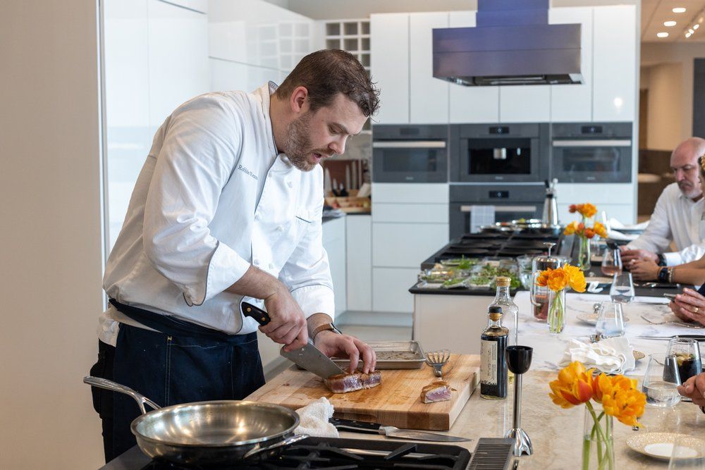 A man is cutting a piece of meat on a cutting board in a kitchen.