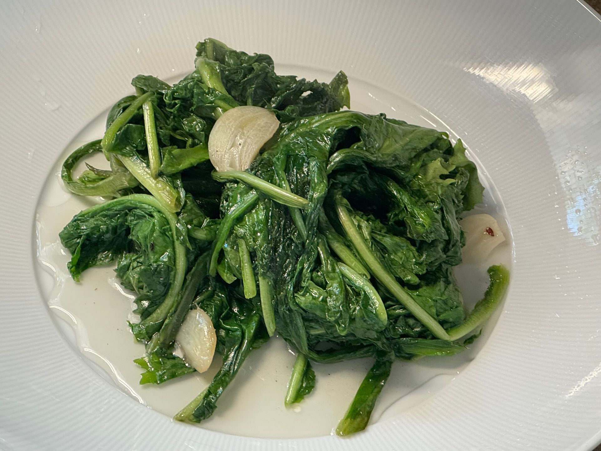 A white plate topped with spinach and garlic.