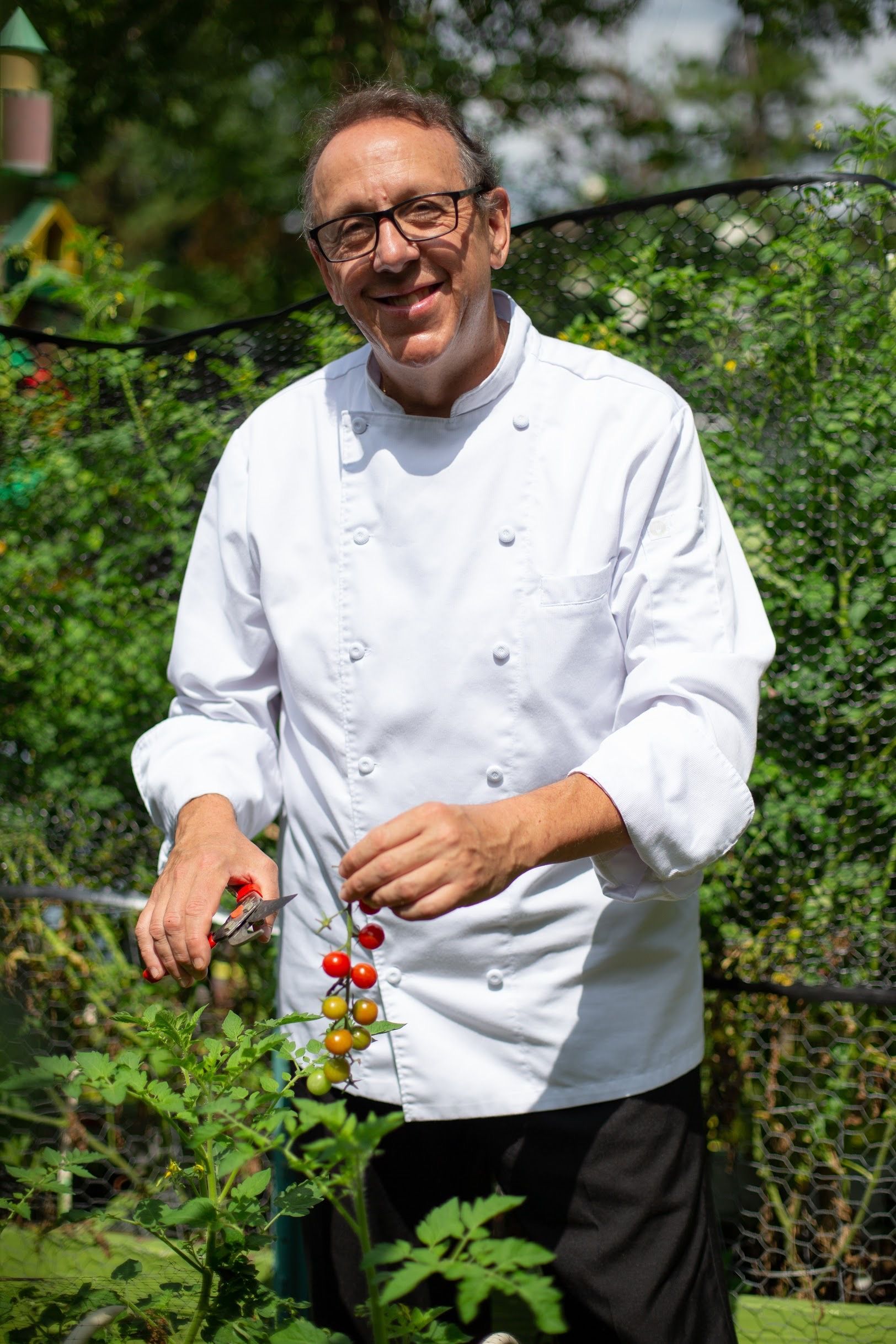 A man in a chef 's uniform is standing in a garden.