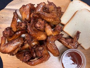 A wooden cutting board topped with chicken wings and bread.