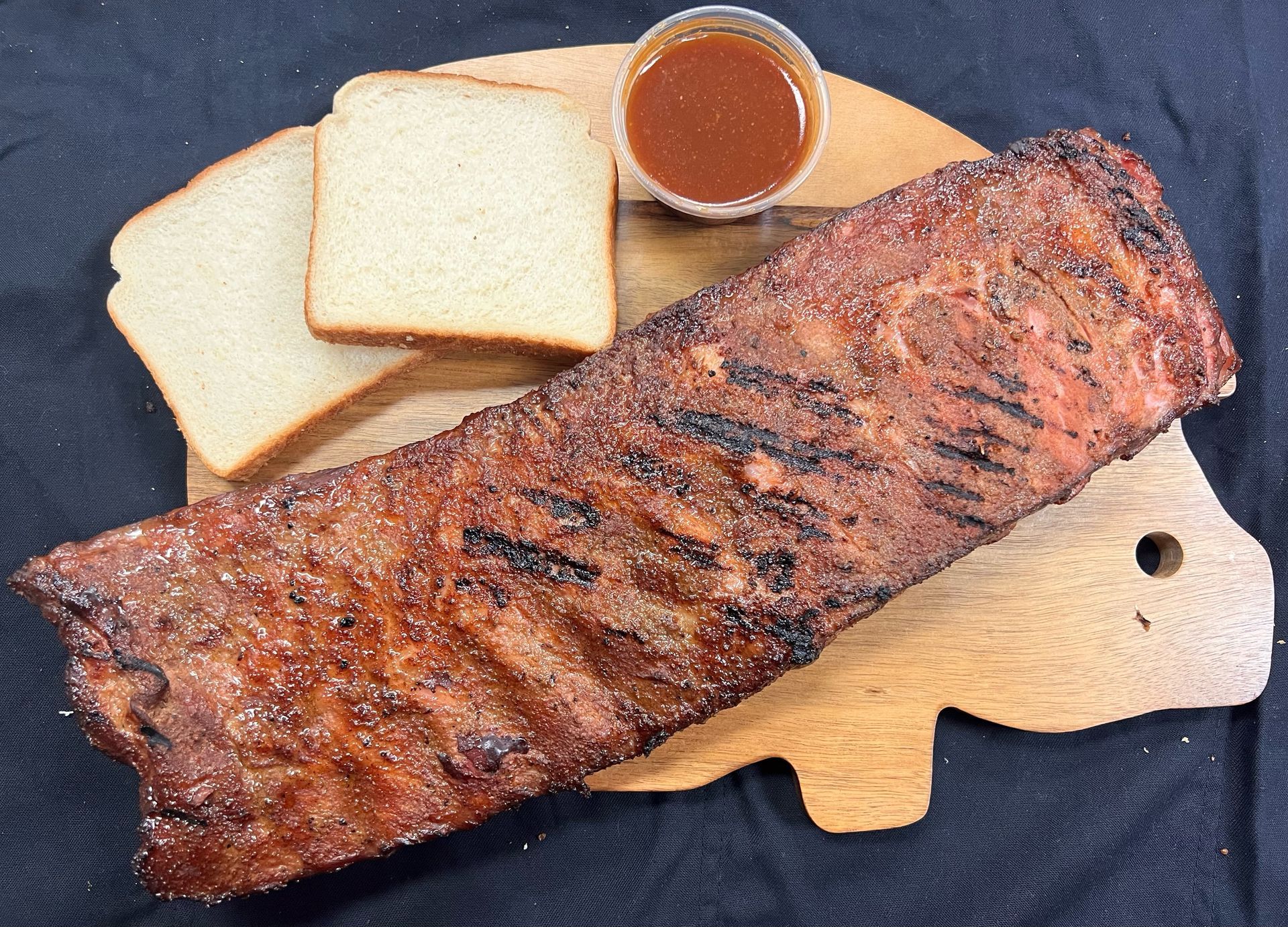 A cutting board with ribs , bread and sauce on it.