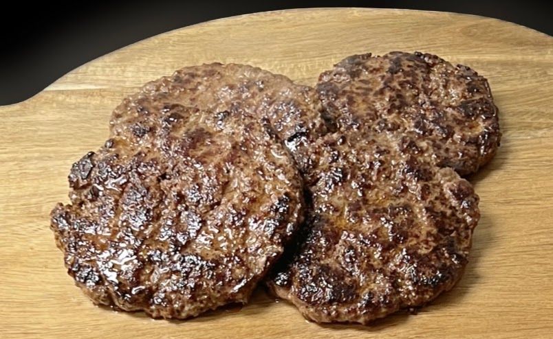 Three hamburger patties are on a wooden cutting board