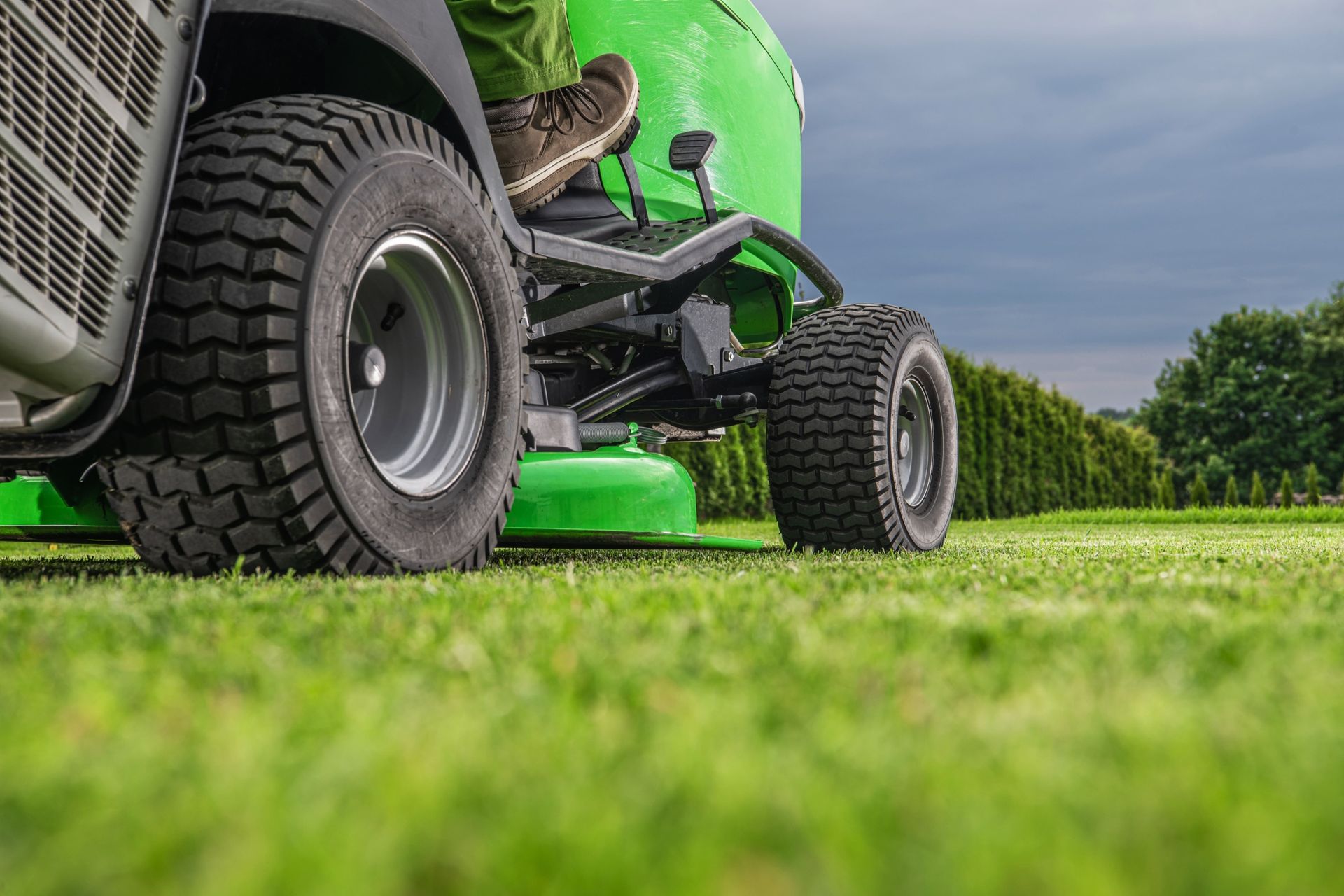 A person is riding a green lawn mower on a lush green field.