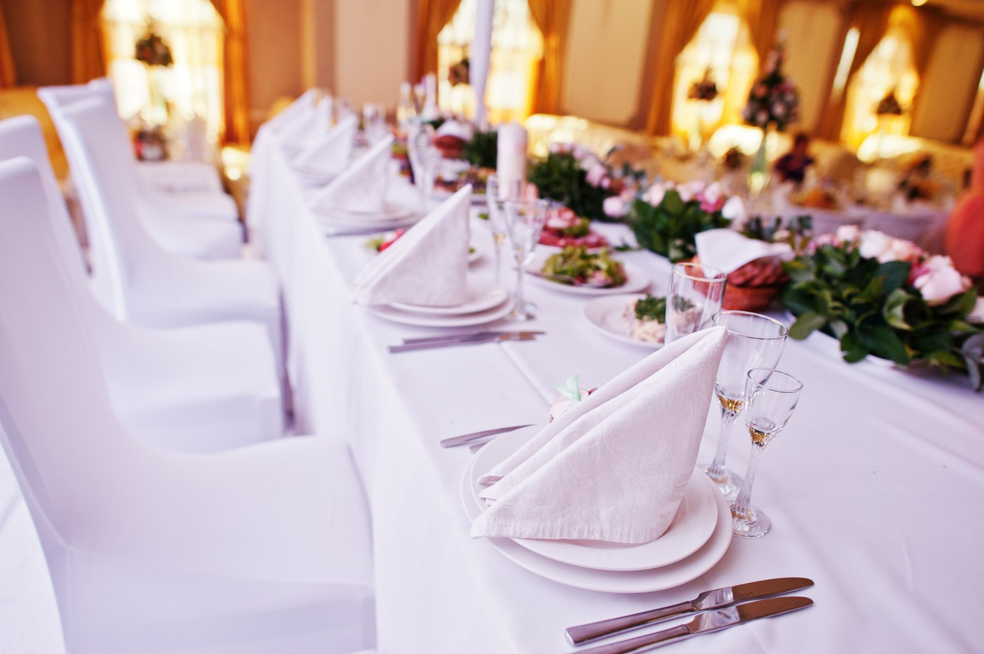 A long table with plates , napkins , utensils and flowers on it.