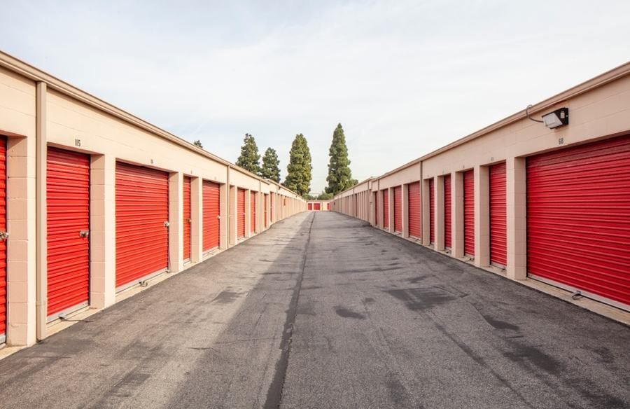 A row of red storage units along a road with trees in the background.