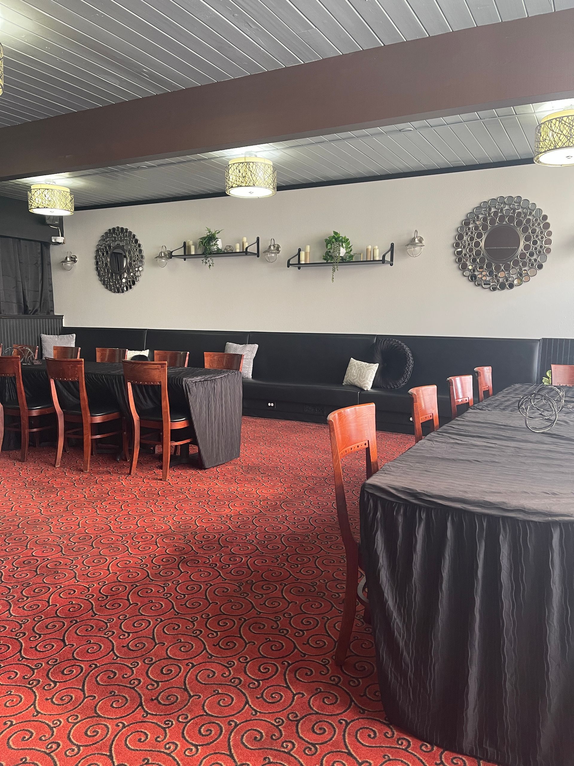 A room with red patterned carpet, black tables and chairs, a dark couch, and decorative wall accents.