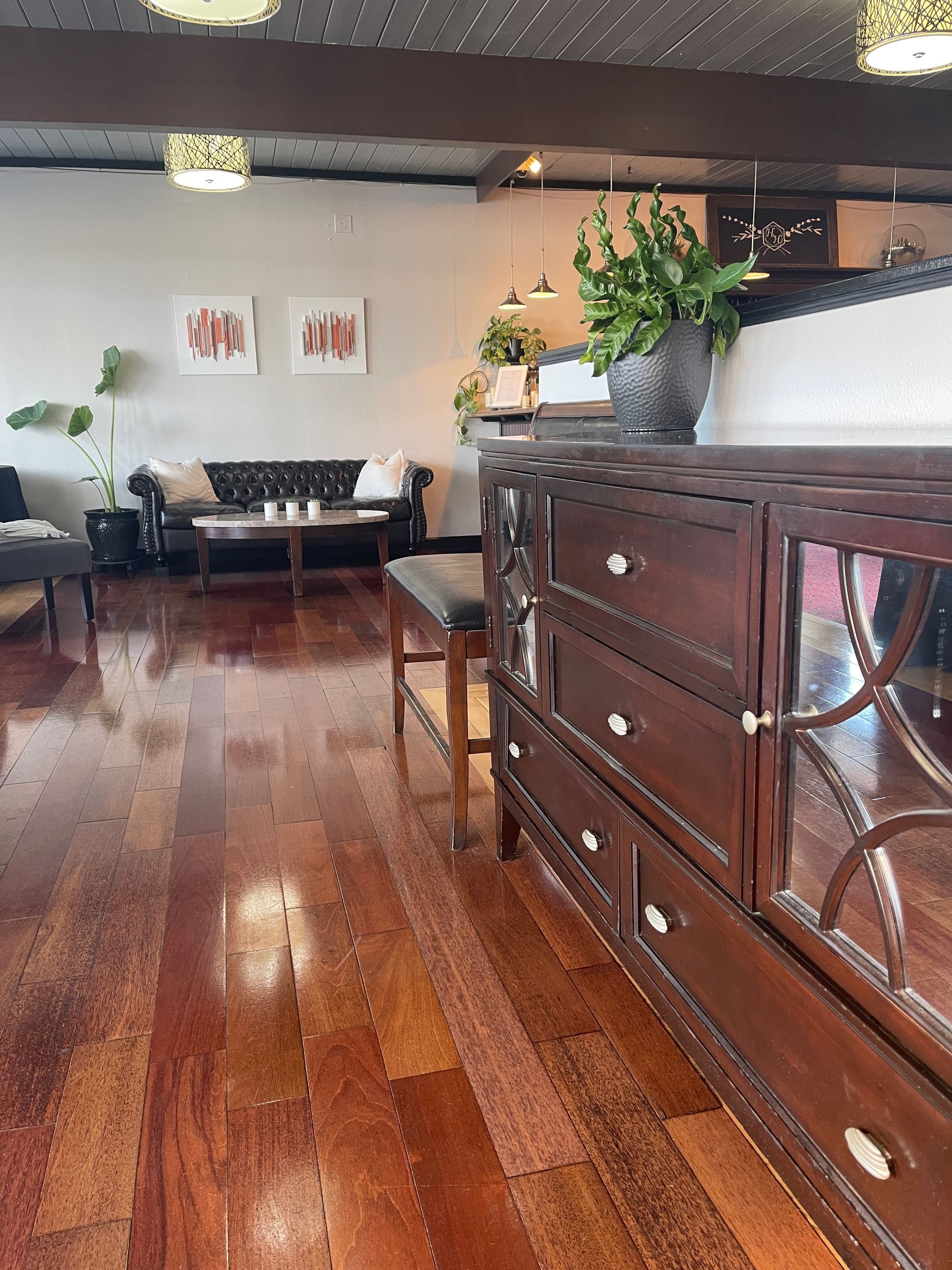 A dark wood dresser in a room with hardwood floors, a couch, and two framed pictures.