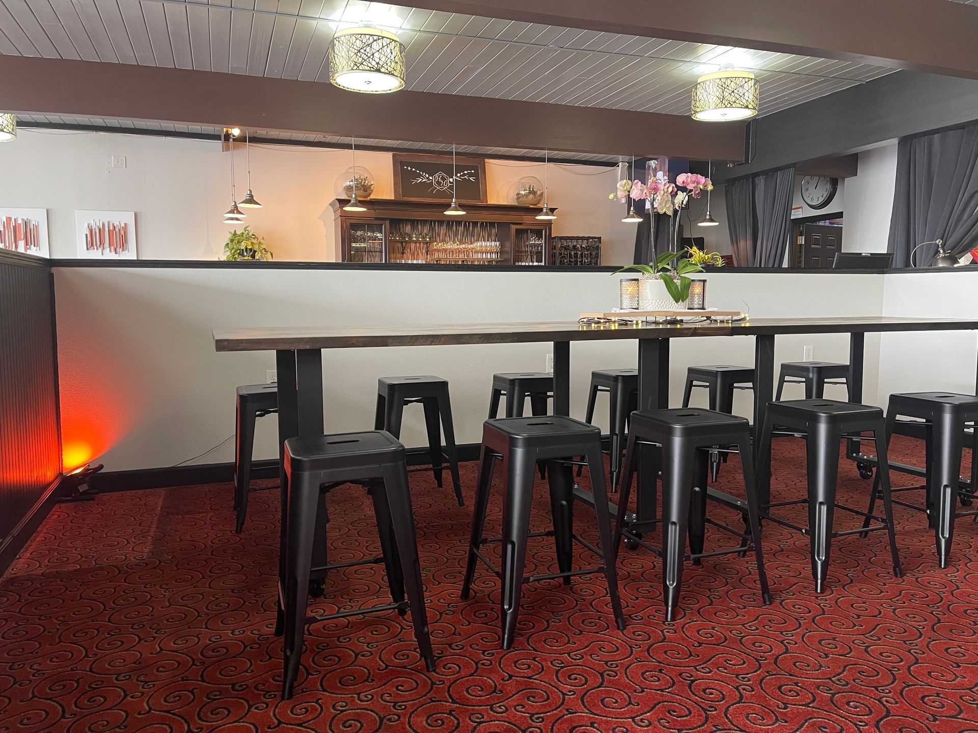 Bar area with high-top table, black stools, red carpet, and decorative lighting.
