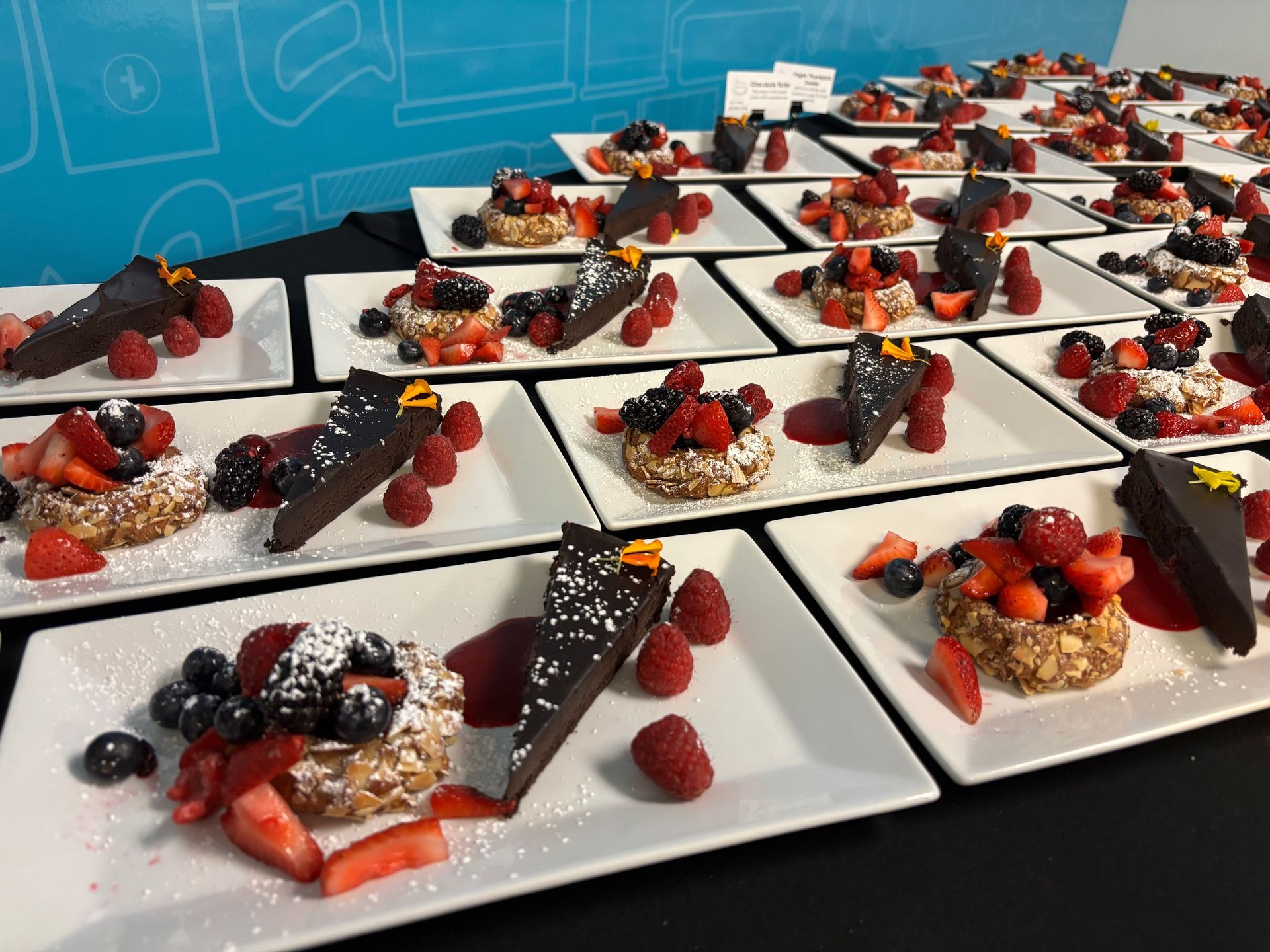 Desserts plated on white squares, each with a slice of cake and berry-topped pastry.