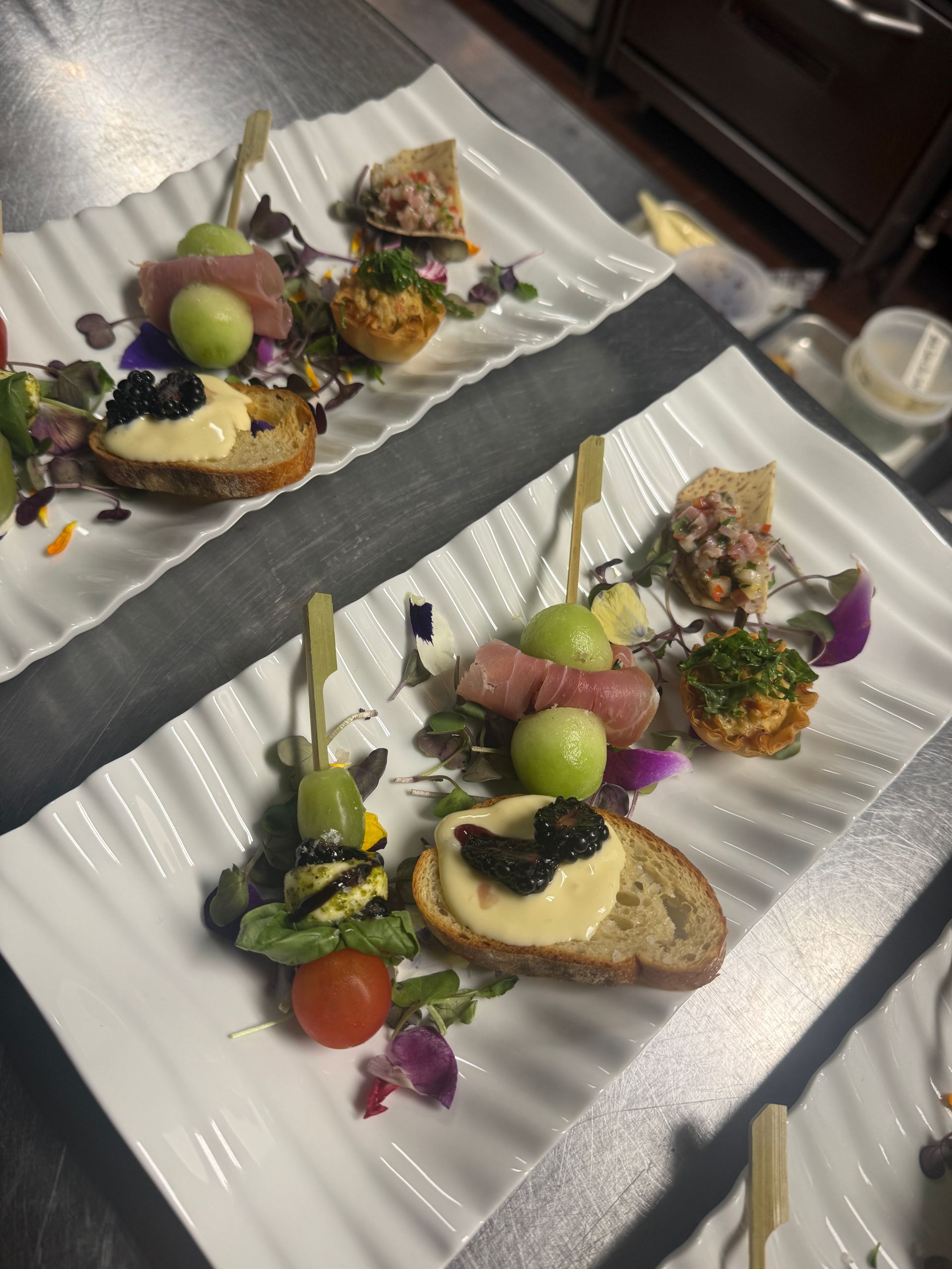 Two plates of appetizers, each with skewers of grapes and prosciutto, and other small bites, arranged decoratively.