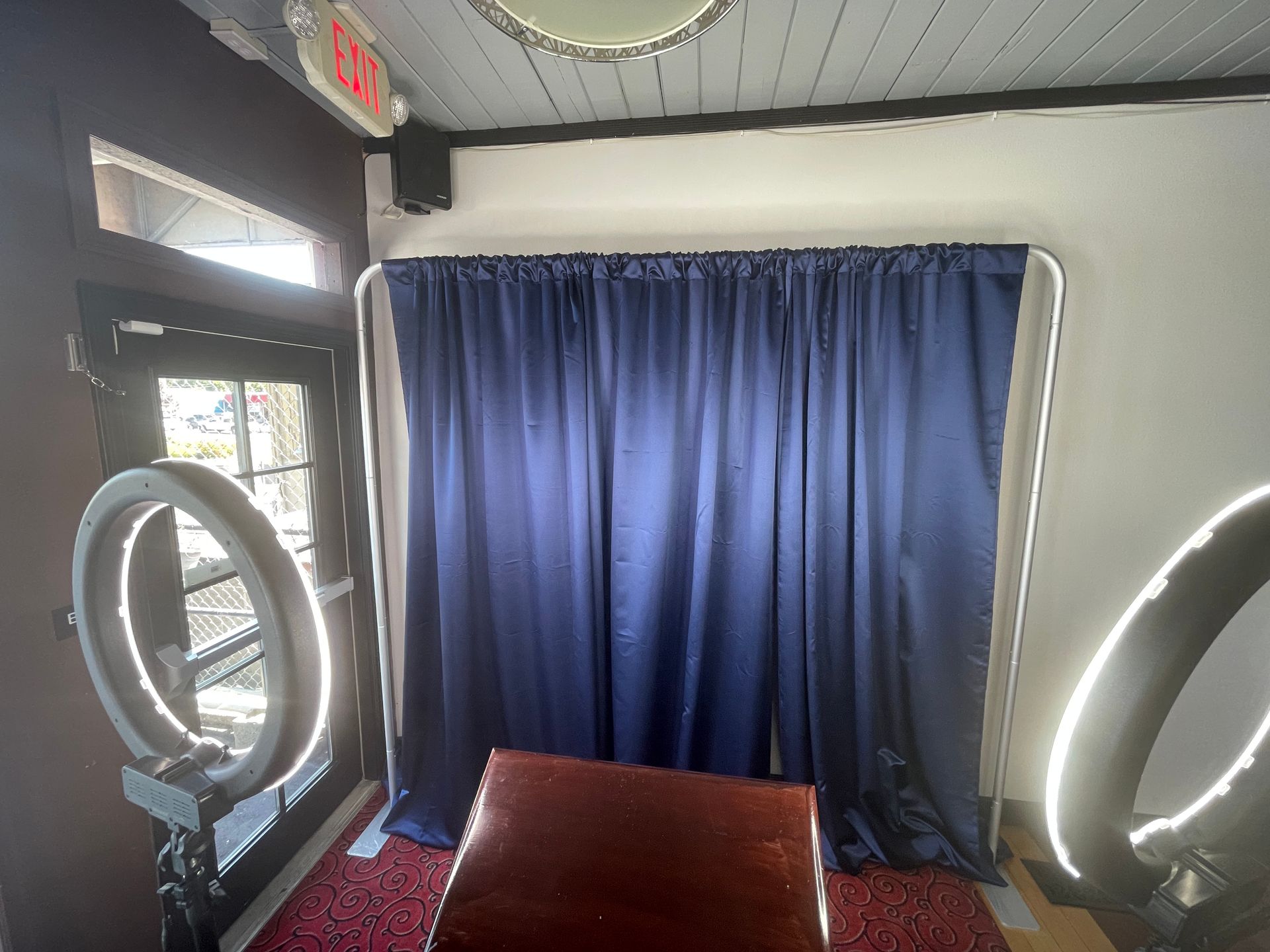 Photo booth setup with blue curtain backdrop, ring lights, and wooden chair.