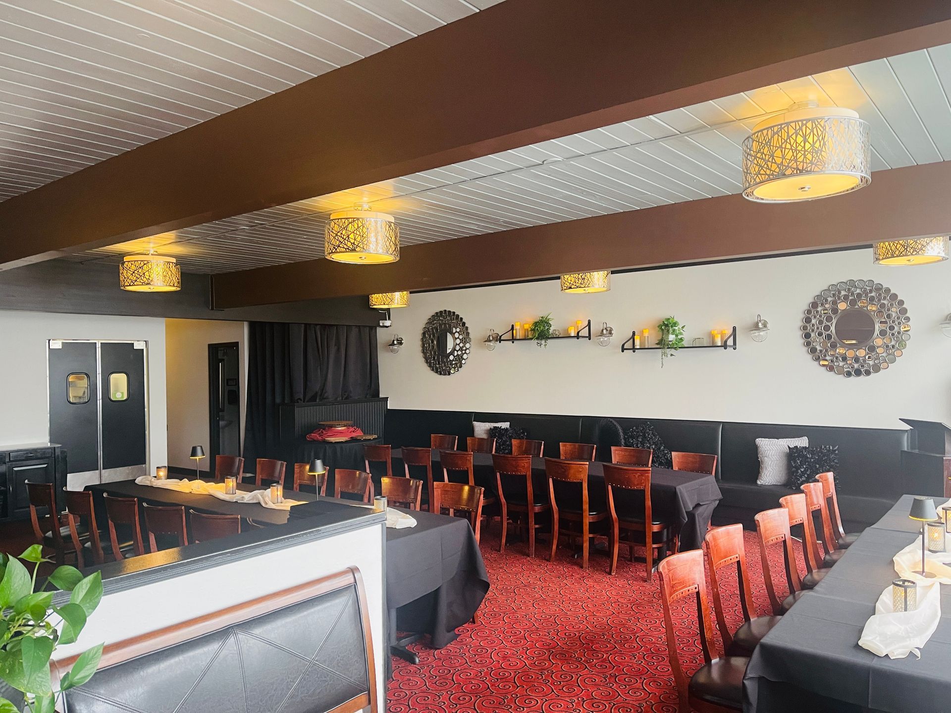Interior event space with tables, chairs, and decorative lighting. Red carpet, dark walls, and black tablecloths.