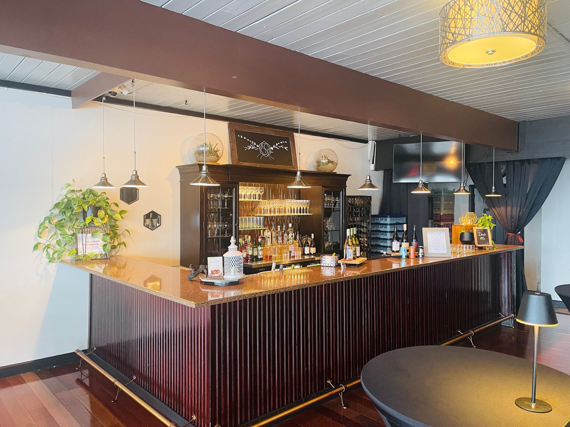 Bar with a wooden counter and shelving, dark red paneling, and hanging lights.