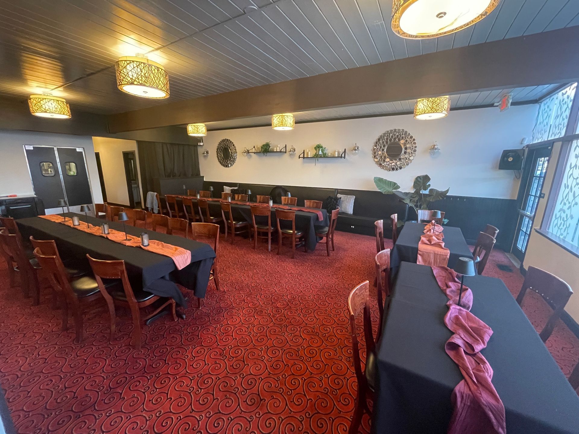 Event room with tables set for a gathering, red carpet, dark tables, and warm lighting.