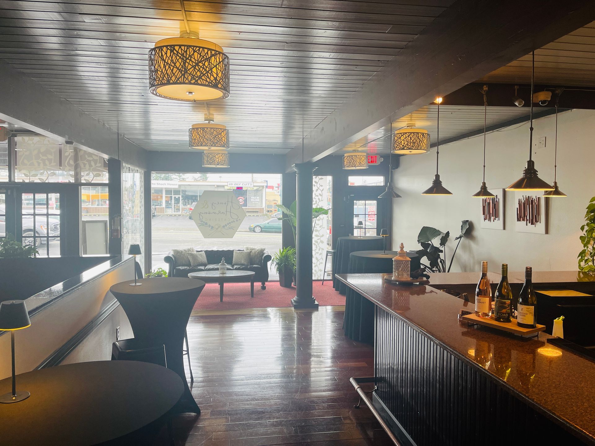 Interior view of a bar with a long counter, tables, and seating area near a large window.