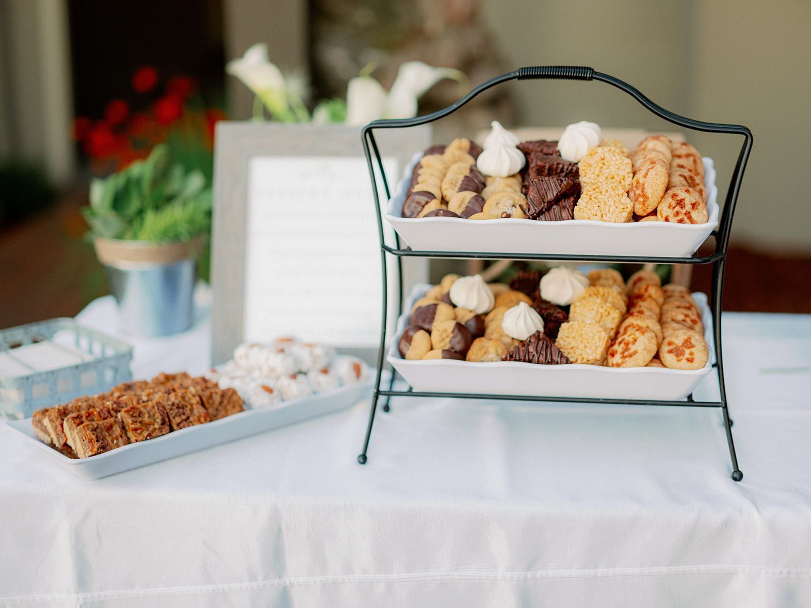 Dessert buffet with tiered stand of cookies, plus other treats on a white table.