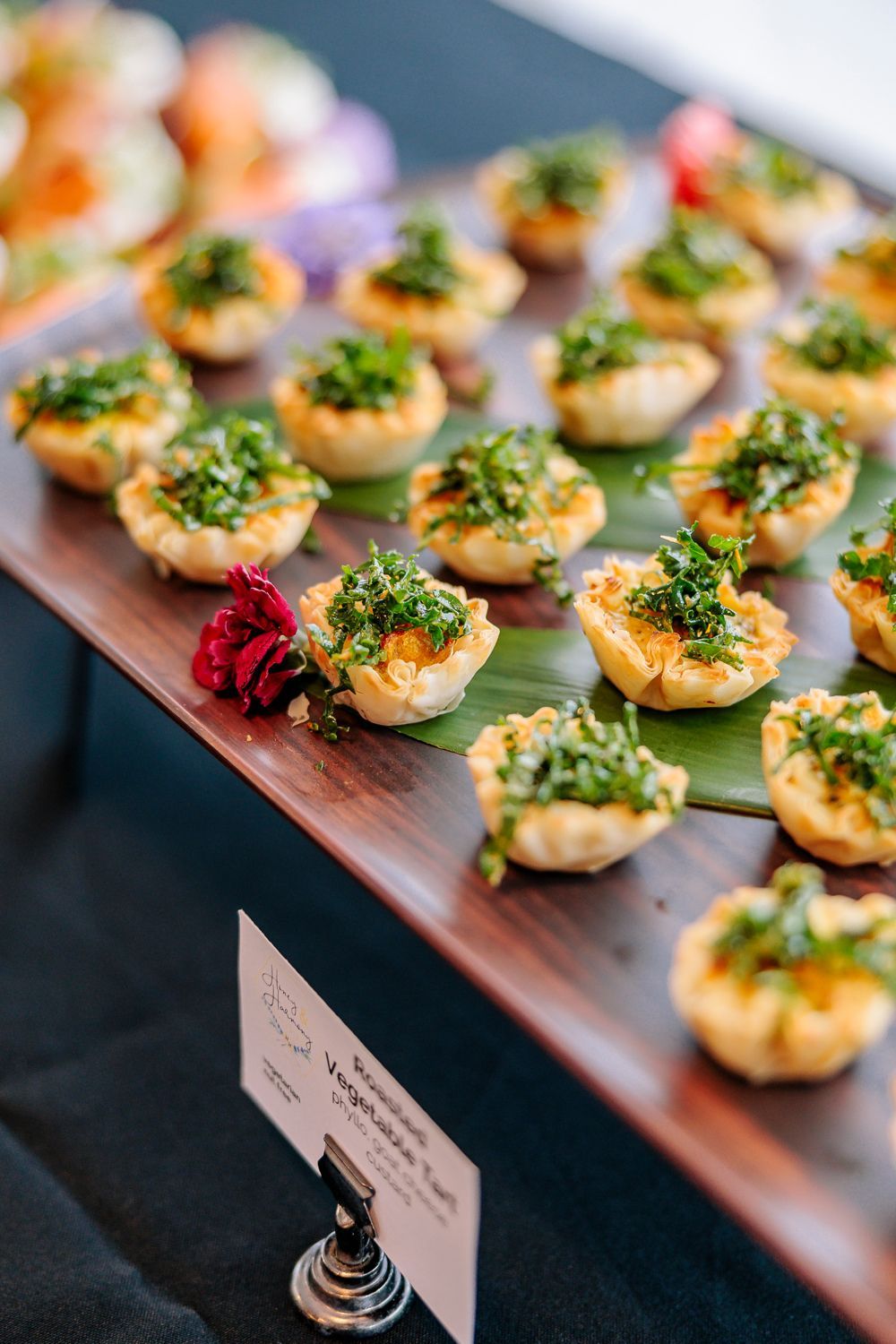 Appetizer tartlets with green topping, arranged on a wooden platter, with a small sign.