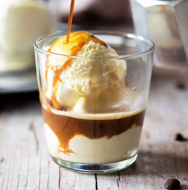Hot espresso is poured over a scoop of creamy vanilla ice cream in a glass on a rustic wooden table.