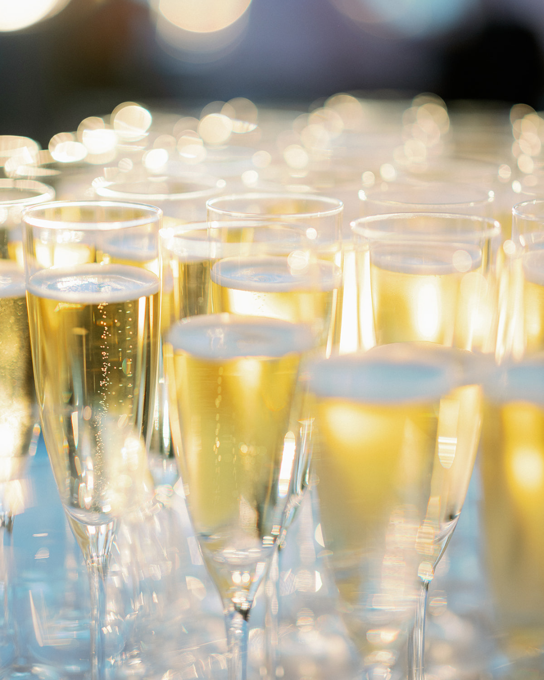 Multiple flutes filled with sparkling golden champagne, arranged on a surface with a soft, out-of-focus background.