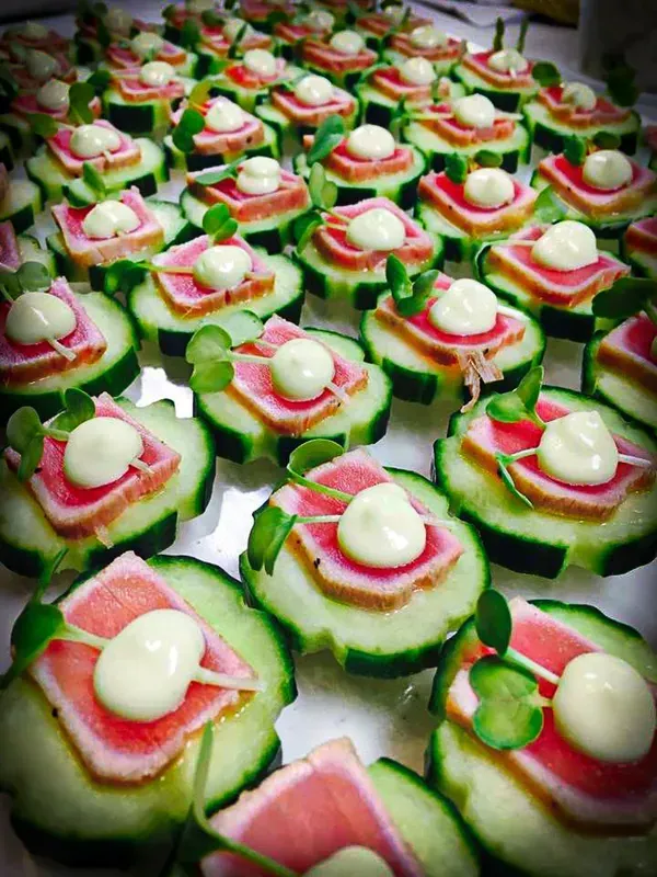 Two cocktails on a bar with a sign. One is red with a lime garnish, the other is purple with a flower.