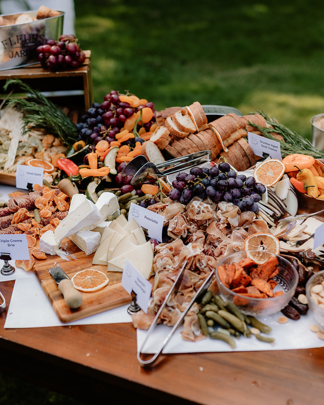 Charcuterie board with grapes, cheese, bread, and various snacks, outdoors.