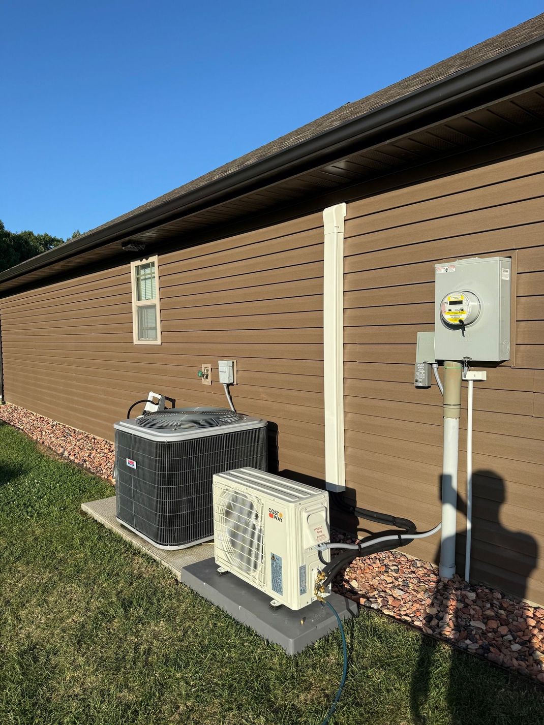 A brown-sided house exterior with two HVAC units sitting on concrete pads next to an electrical meter box.