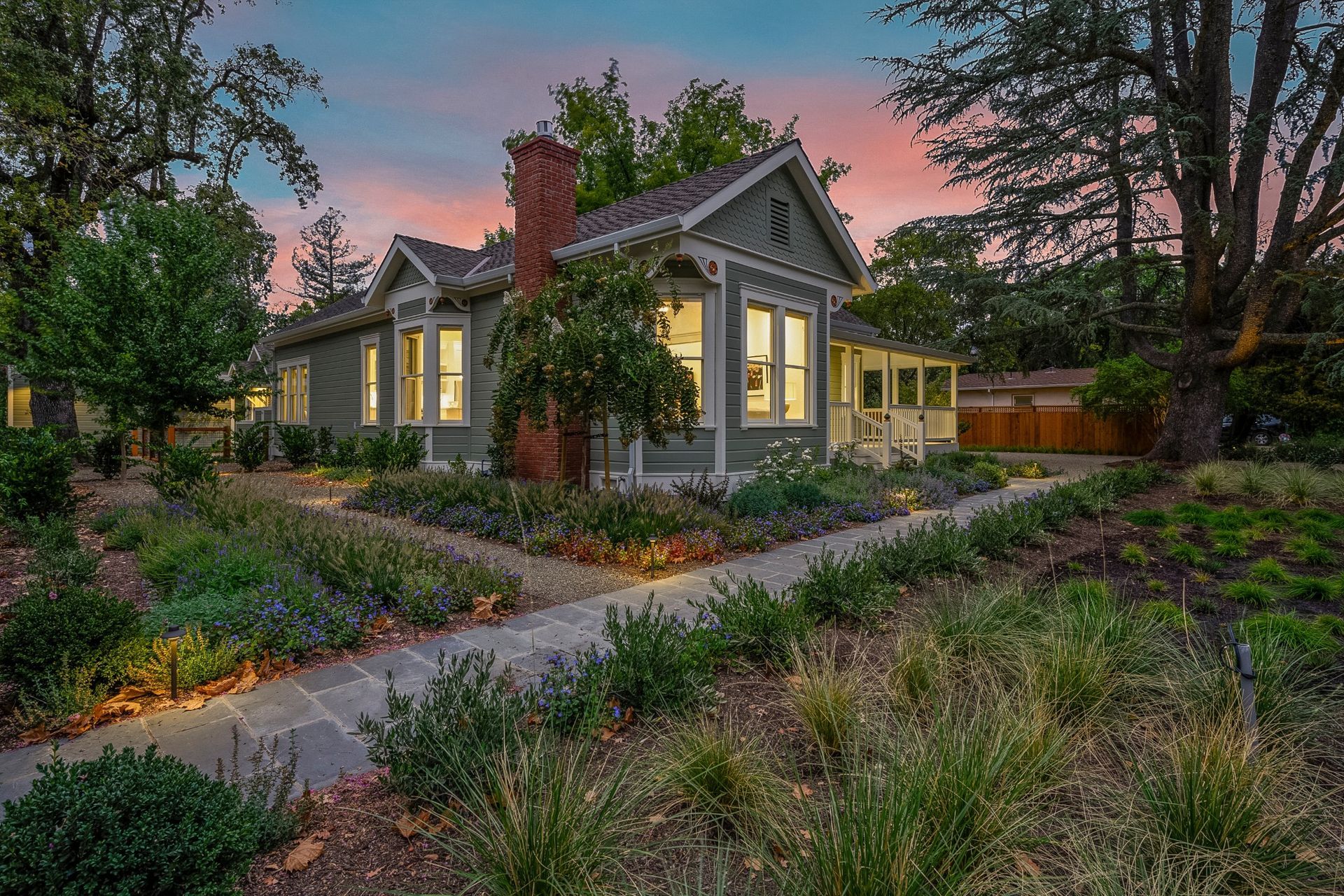 A house with a walkway leading to it is surrounded by trees and bushes.