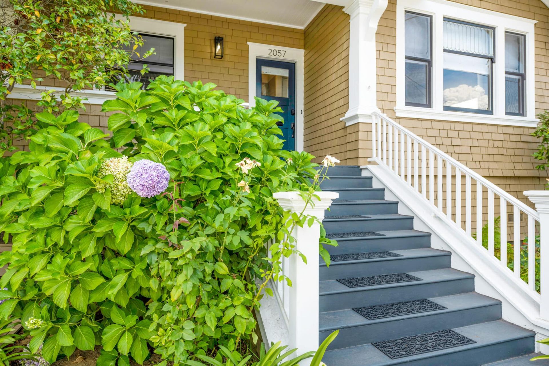 A house with stairs leading up to the front door surrounded by plants and flowers.
