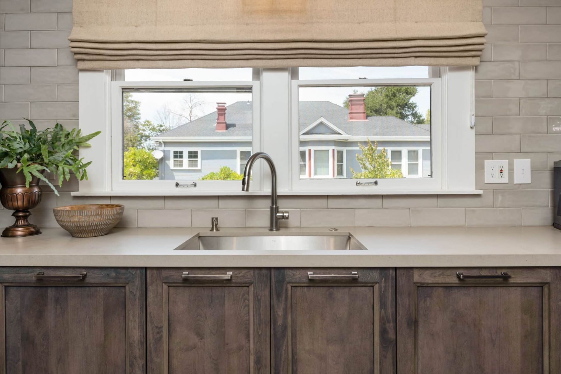 A kitchen with a sink and a window with a view of a house.