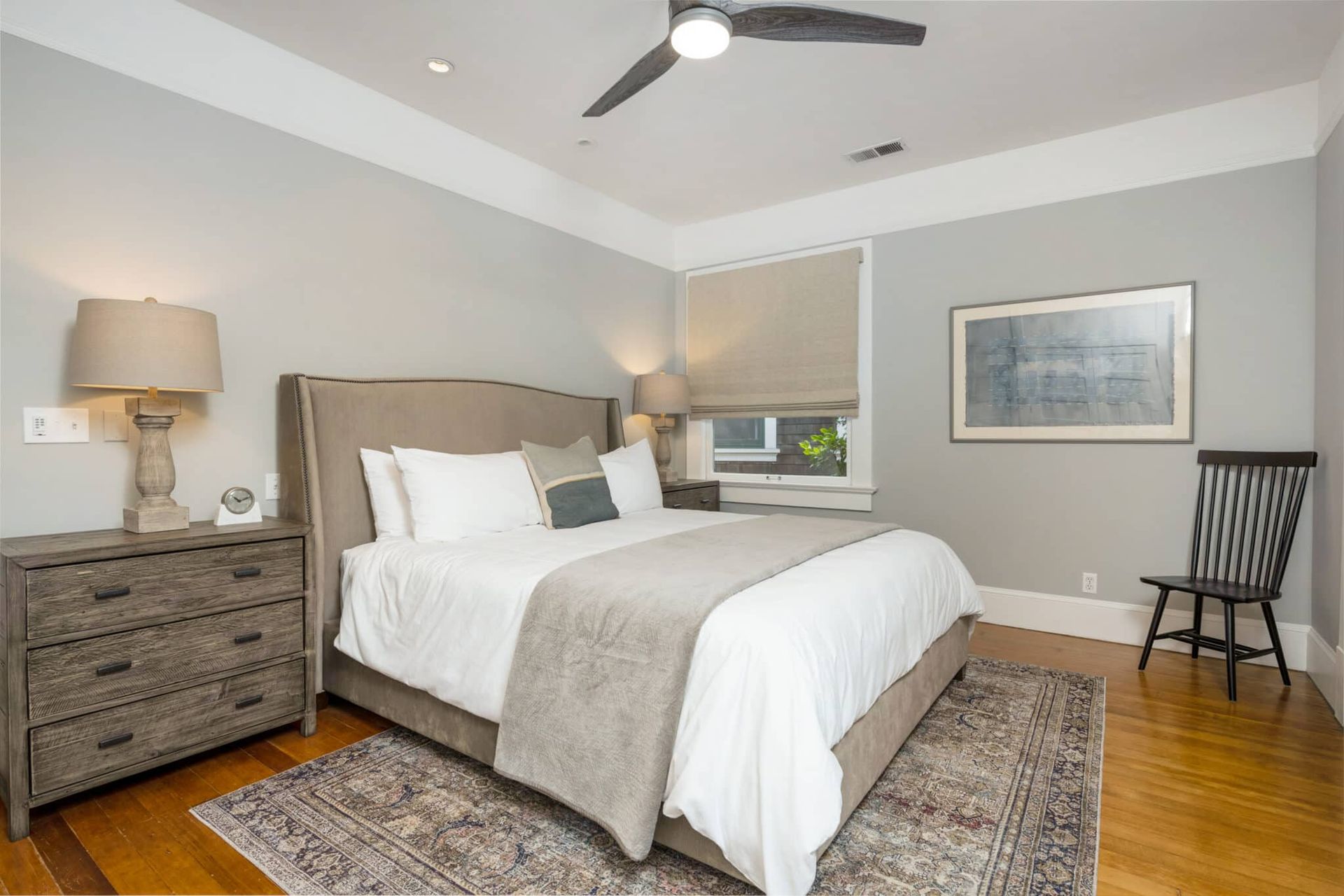 A bedroom with a bed , dresser , chair and ceiling fan.