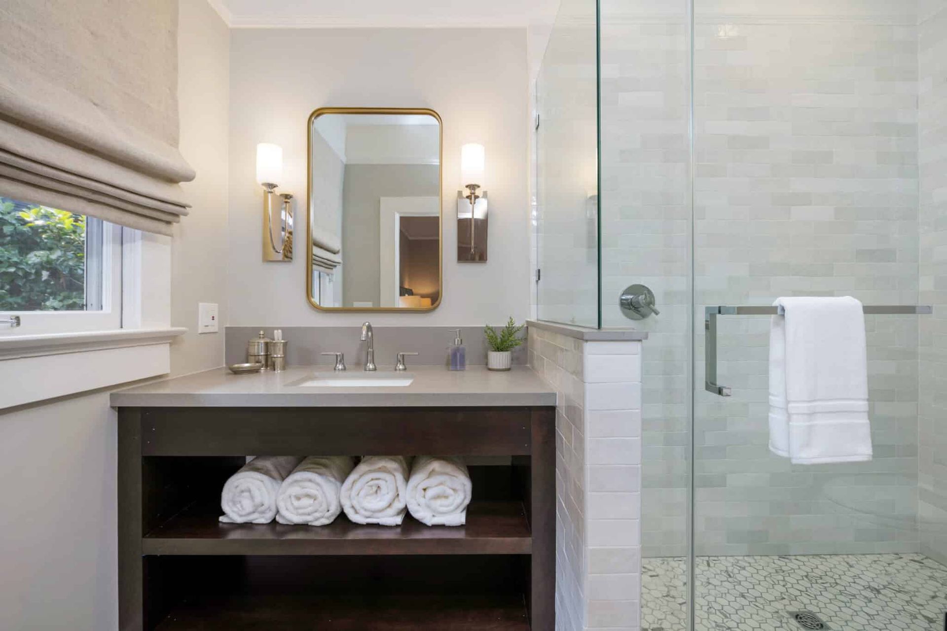 A bathroom with a sink , mirror , towels and a walk in shower.