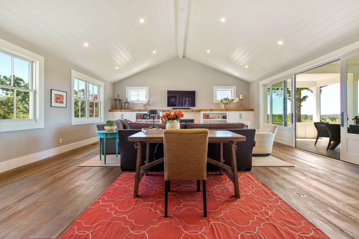 A living room with a vaulted ceiling and a table and chairs.