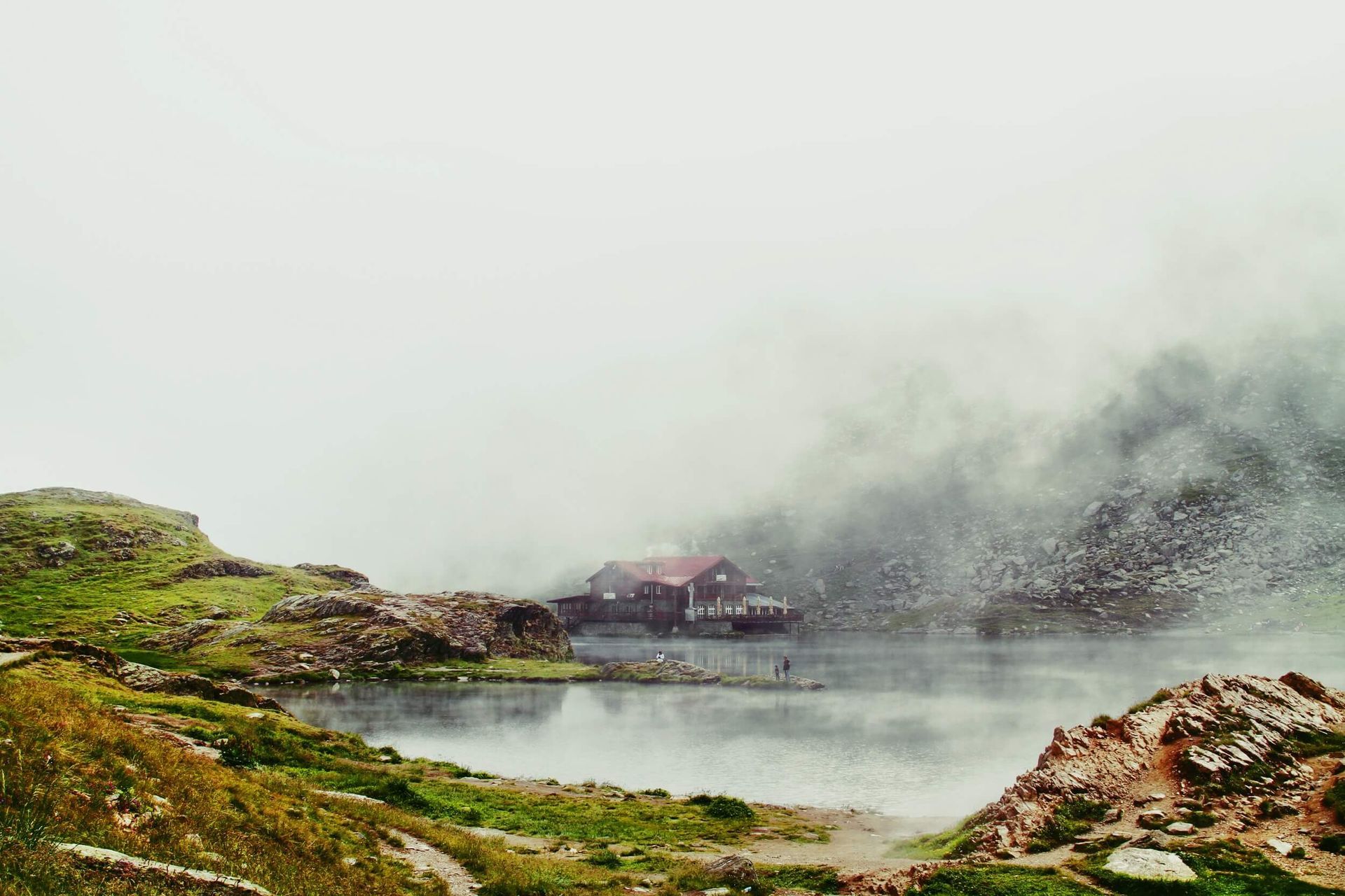 A small house is sitting on the shore of a lake surrounded by fog.