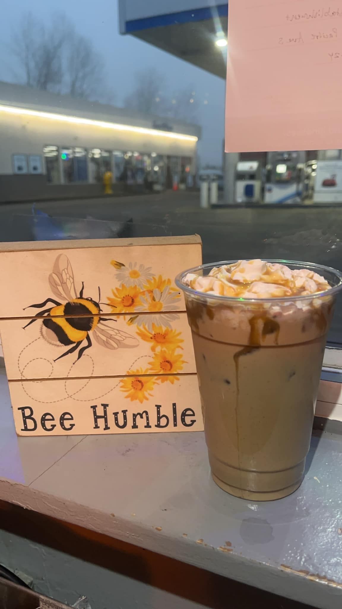 A cup of coffee is sitting on a table next to a sign that says bee humble.