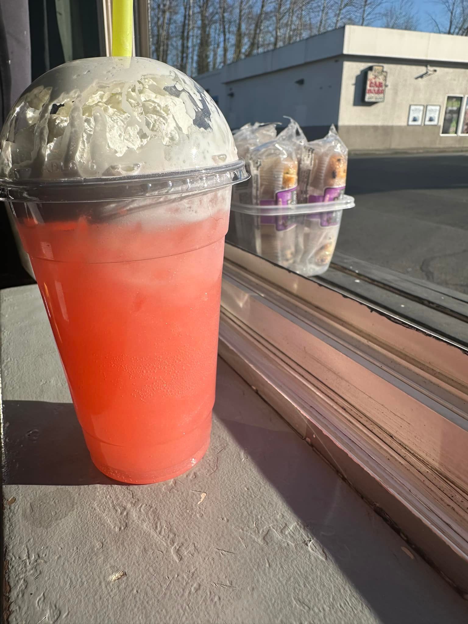 A cup of pink liquid is sitting on a window sill next to a window.
