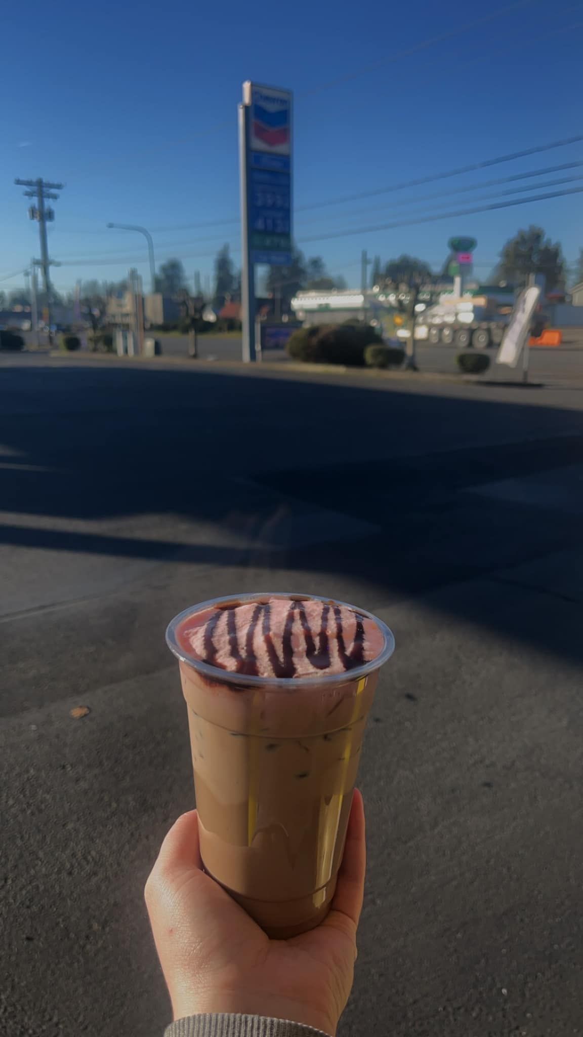 A person is holding a cup of chocolate milkshake in front of a pepsi sign.