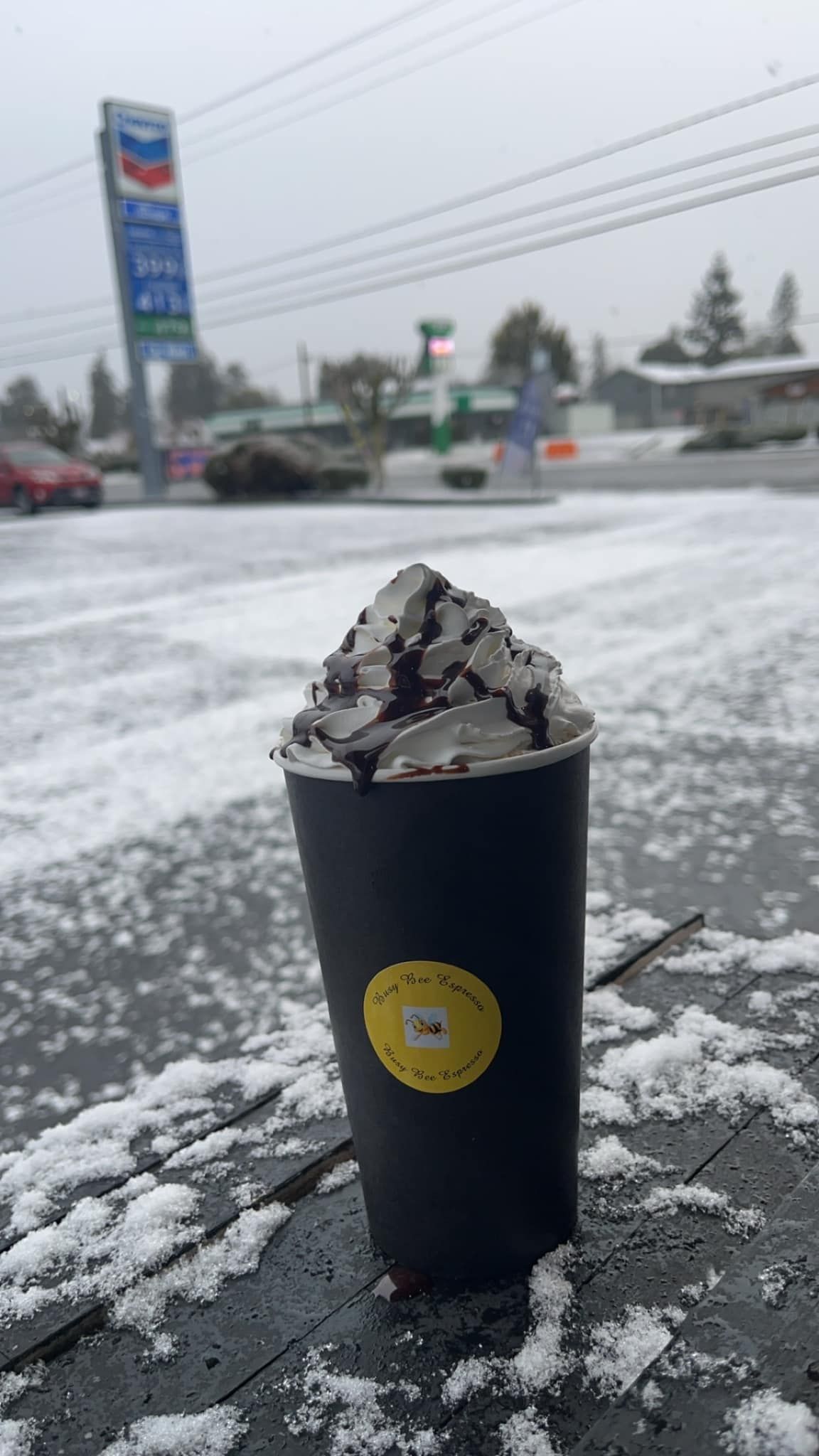 A cup of coffee is sitting on the side of the road in the snow.