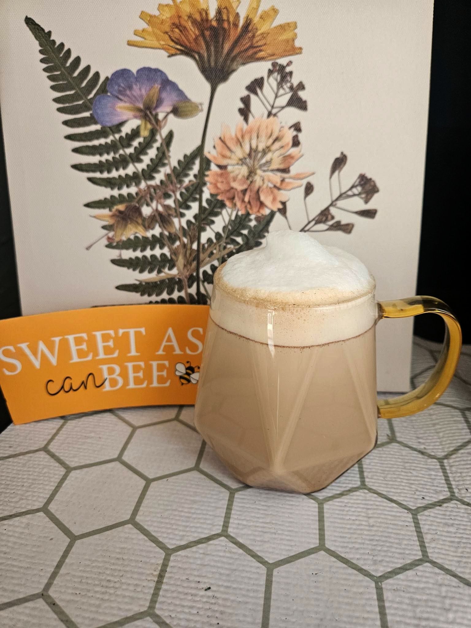 A cup of coffee sits on a table next to a sign that says sweet as can bee